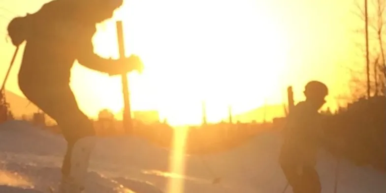 A picture of two skiers with a sunset as a backdrop.