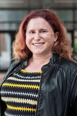 Smiling woman with long red hair wearing a black leather jacket.