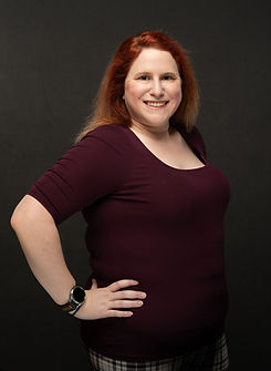 Middle aged woman in purple, hands on hips, smiling