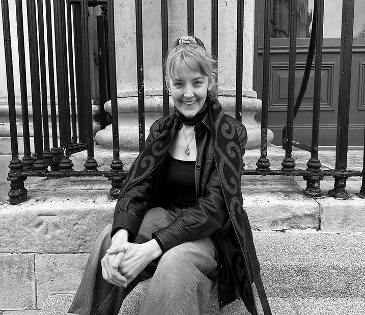 A picture of writer Elizabeth Oxley seated on stone steps and smiling.