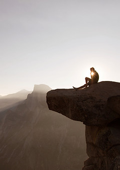 A man sitting on the cliff edge looking out at the view and distance