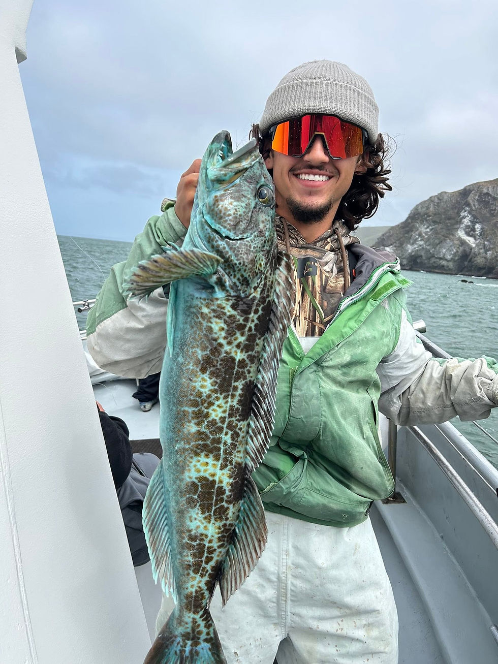 Angler on a boat holding a large blue lingcod.