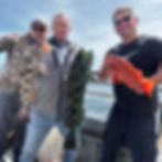 Three men holding fresh lingcod and rockfish on a boat.