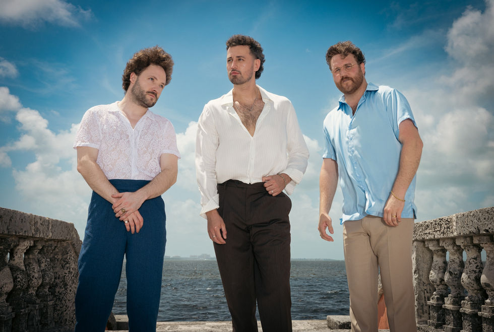 Raynes members Mat Charley, Mark Race, and Joe Berger stand in front of the ocean and sky.