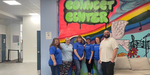 Six volunteers in blue shirts by a Connect Center mural