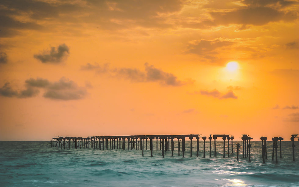 Orange sunset over a vast ocean, silhouettes of a weathered pier extend into the water, creating a serene and peaceful atmosphere.