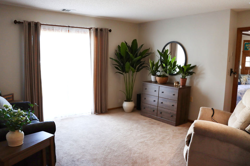 Large well-lit living room in a senior living apartment with large sliding doors opening to an outdoor patio at Kinship Pointe Seward