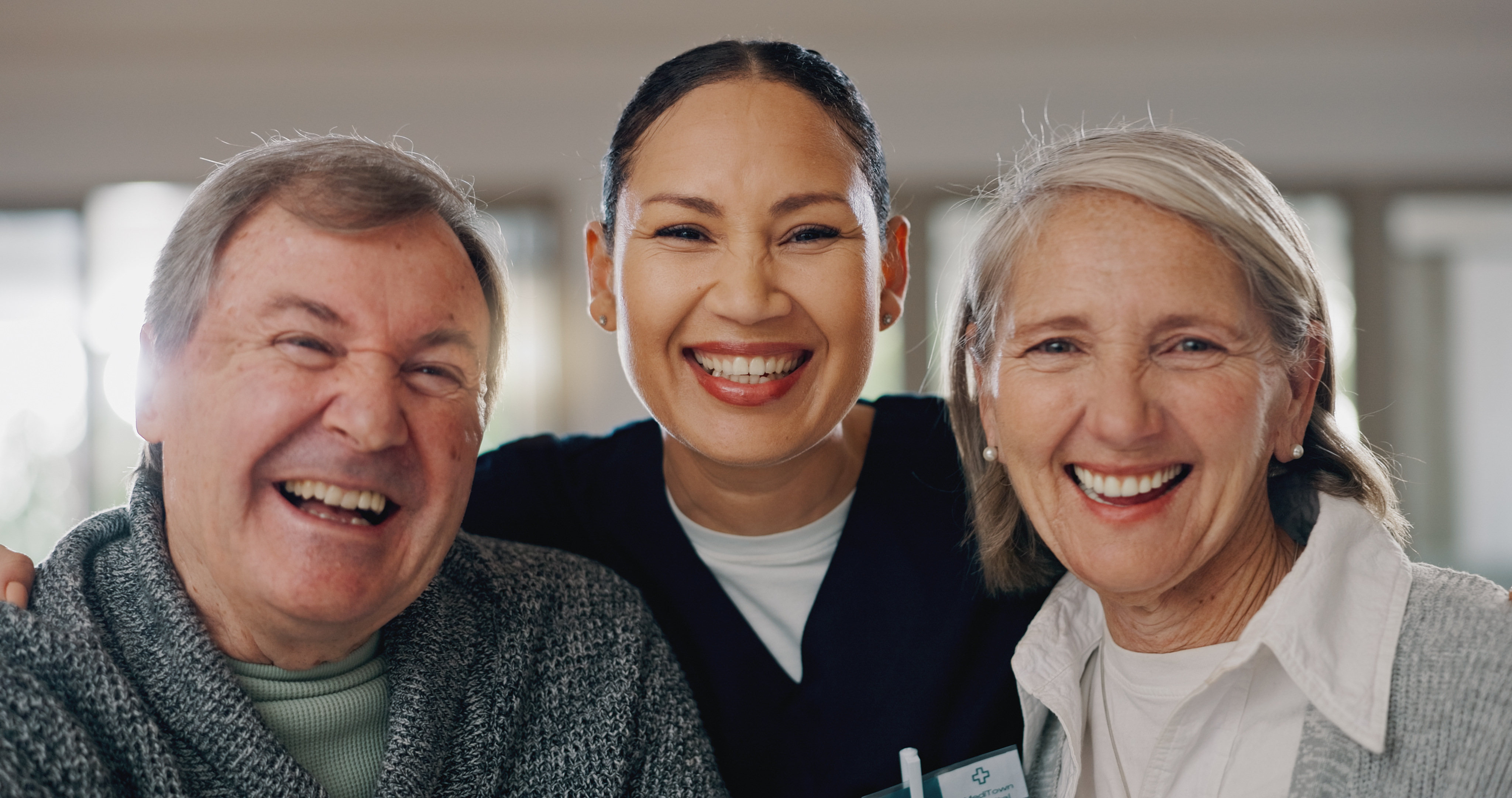 An adult daughter and her senior mother laughing together in a sunlit, barrier-free common area at Kinship Pointe Seward assisted living.
