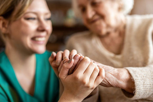 A female caregiver holding the hands of an elderly woman with dementia