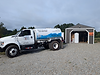 L&M Water Services delivery truck parked outside a utility building equipped with water storage tanks and treatment equipment.