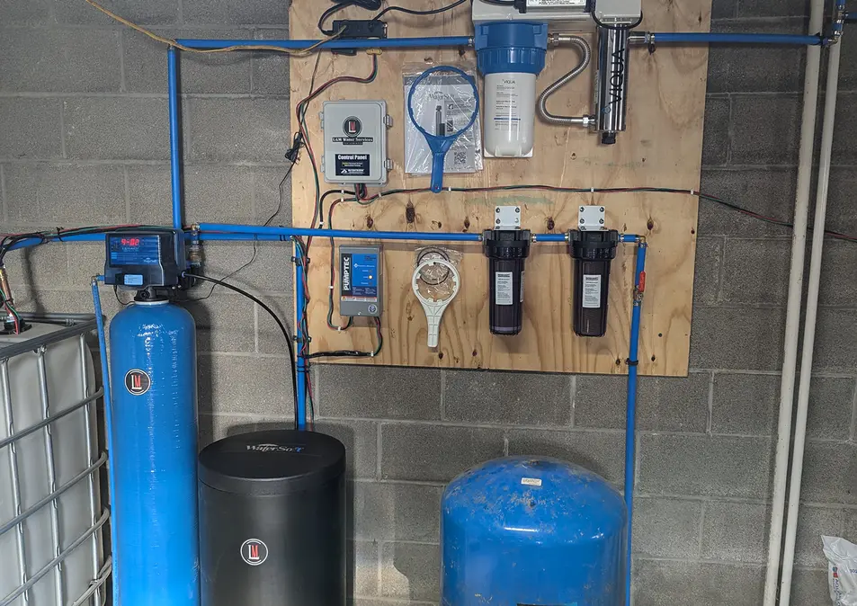 Basement water treatment system installed, featuring a pressure tank, water softener, filtration units, and UV purification system.