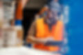 A warehouse worker wearing a high-visibility vest and a headset uses a tablet to manage inventory.