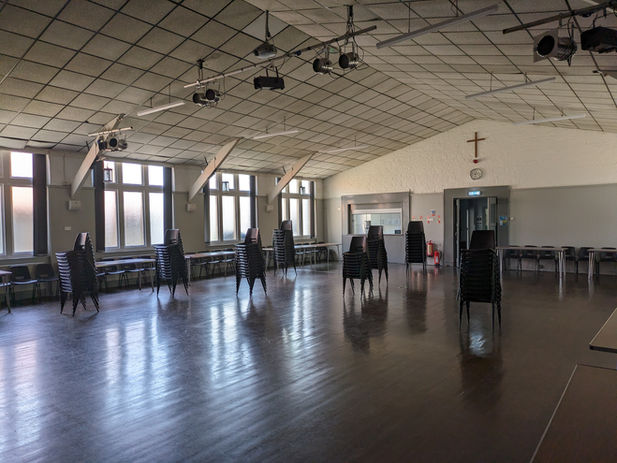 Image of The Main Hall inside Turner Hall, looking towards the entrance on an angle, with stacks of chairs dotted around the hall
