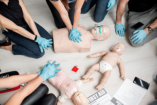 Group of people learning how to make first aid heart compressions with dummies during the