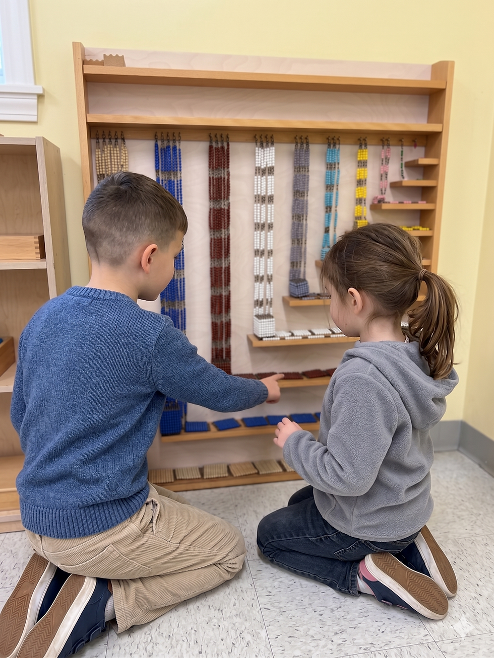 Two children kneel in a classroom and point at colorful Montessori bead chains on wooden shelves, focused and curious.