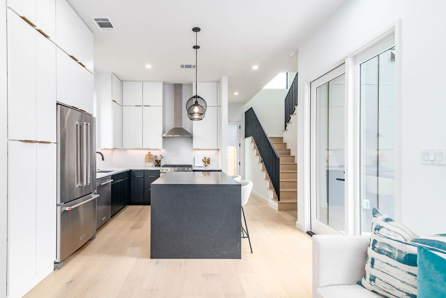 Modern kitchen with dark island, light floors, and staircase