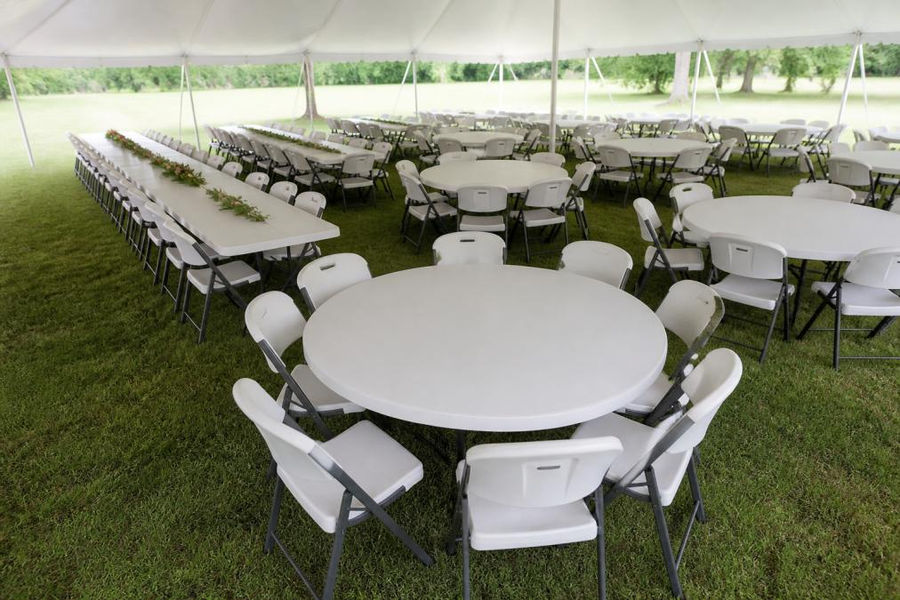 Aerial or elevated view of a tent setup displaying multiple table configurations with chairs arranged for a wedding reception or formal outdoor gathering