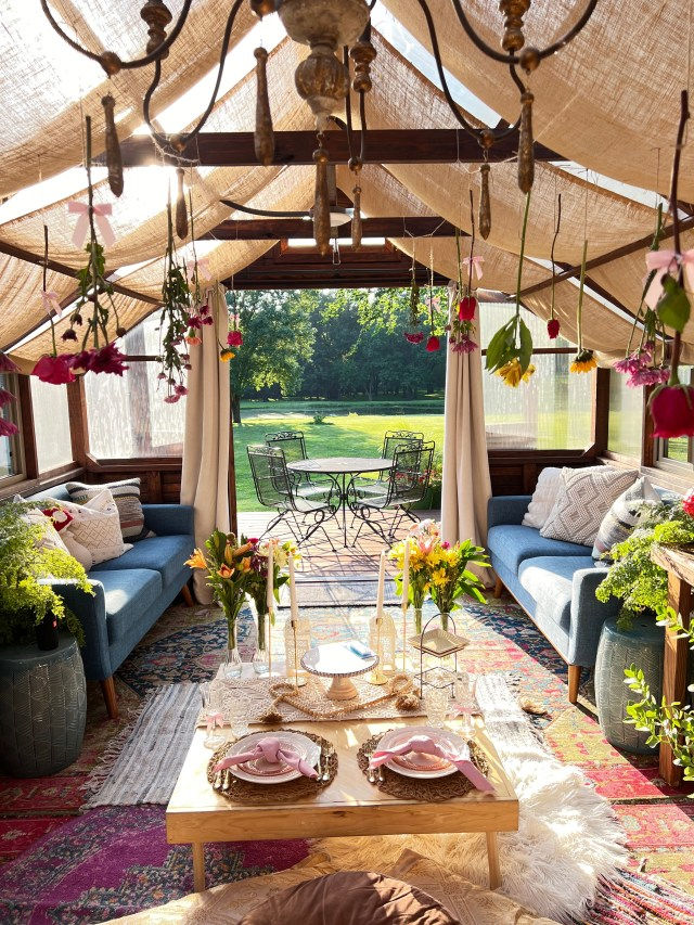 An inviting indoor picnic setup featuring colorful flowers, plush seating, and elegant table decor, with a view of green grass and outdoor seating visible through the window.