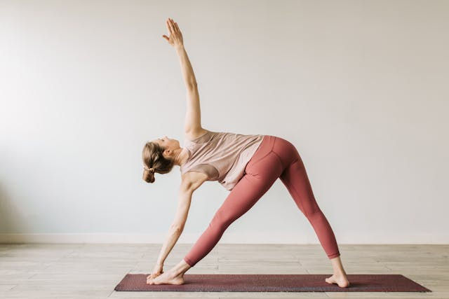 Person in Triangle Pose, one hand reaching down to the shin with the other arm extended upwards, stretching the sides and chest.