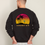 Thumbnail: A man wears jeans and a black crewneck sweatshirt with a sunset and palm tree beach scene on it.