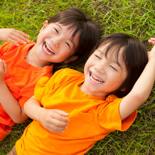 Two happy children in orange shirts are lying on the grass, laughing together.