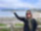 Image of Erin in Vancouver, Canada wearing a black, long-sleeve shirt with a green plaid scarf and sunglasses with her arm raised up, palm-facing up.