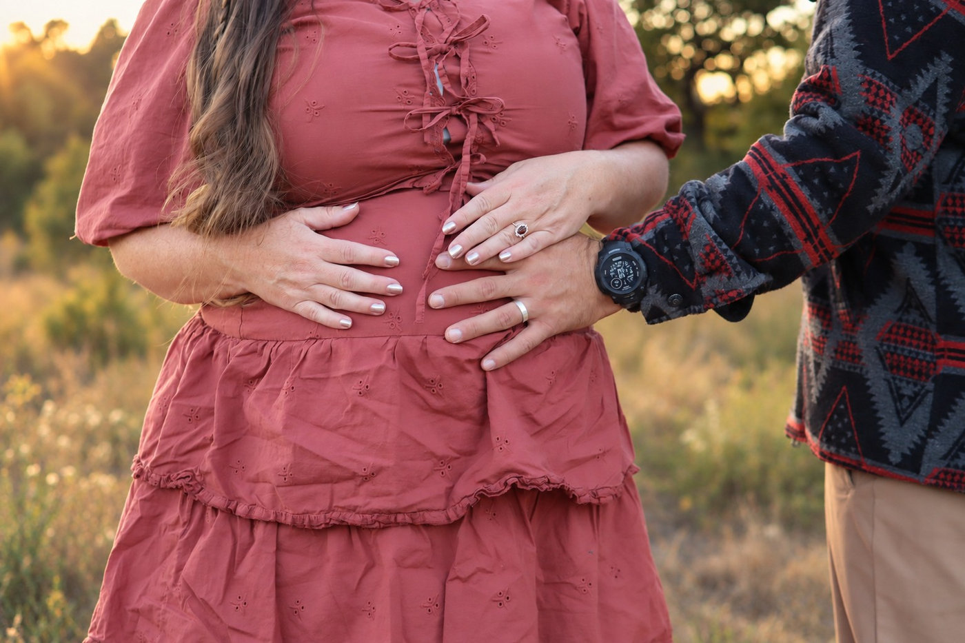 A maternity detail with parents’ hands resting on the belly.