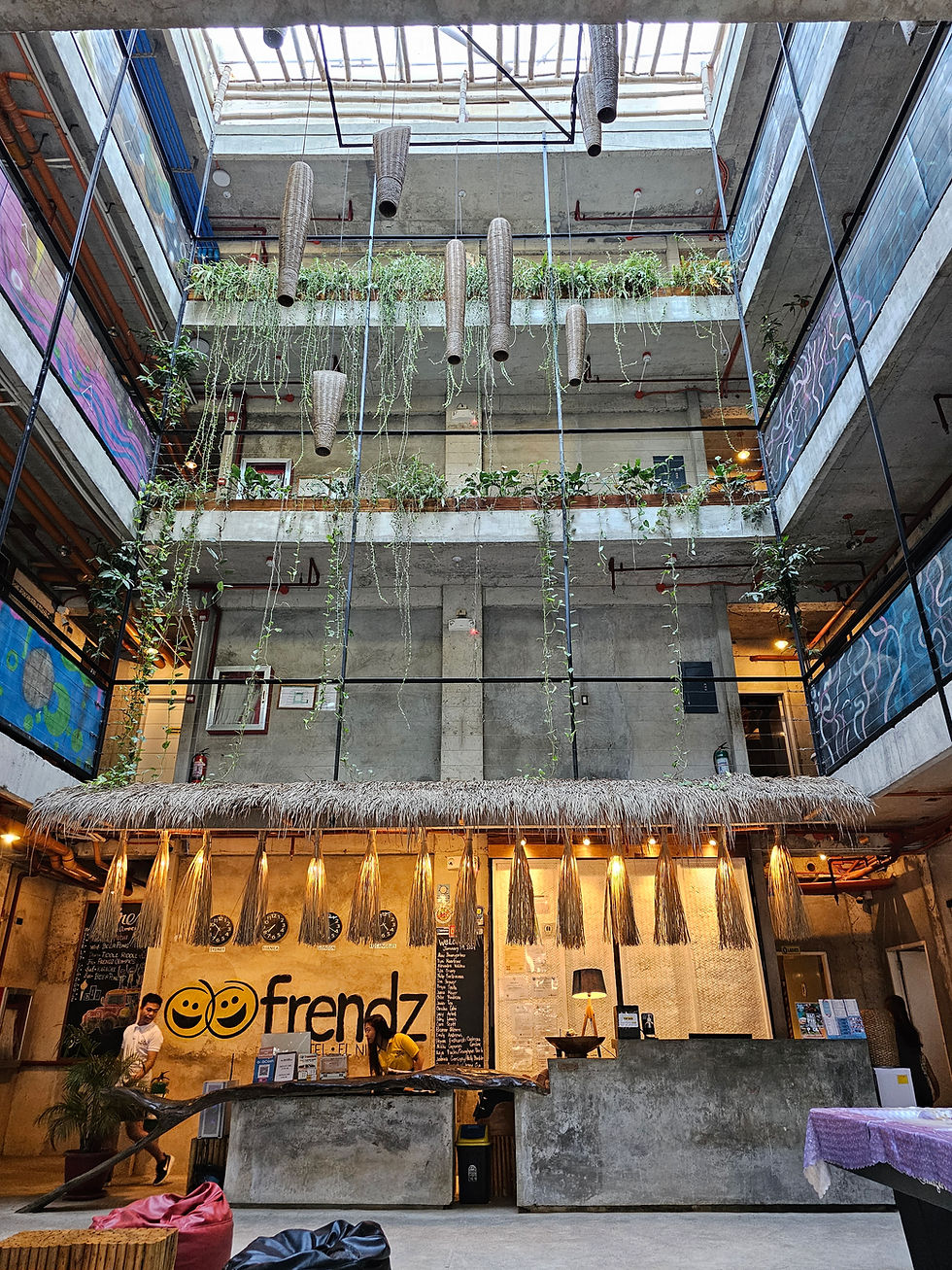 Lobby of a modern building with greenery and hanging decor. "Frendz" logo on the wall. Two people interacting at the reception desk. In Frendz Hostel El Nido