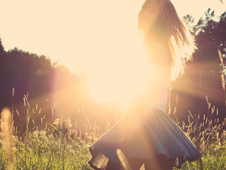 Una persona alegre que hace contraste con la luz solar en un atardecer, en un prado con un bosque de fondo.