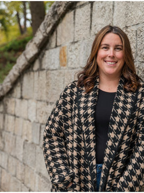 Headshot style photo of a woman leaning her shoulder onto a stone wall.