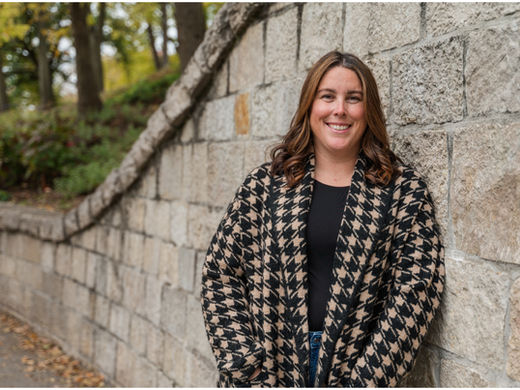 Headshot style photo of a woman leaning her shoulder onto a stone wall.