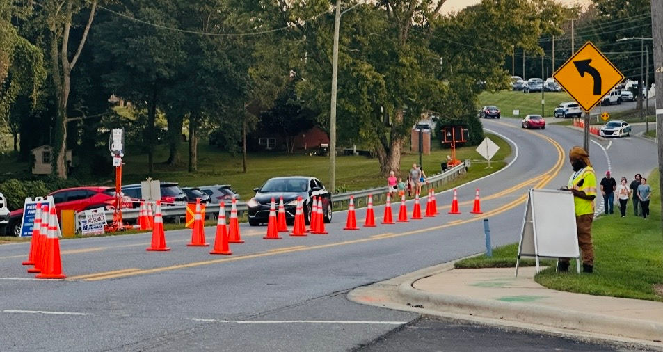 A car waits in the westbound lane on E. Marion Street for the man in the yellow vest to raise the gate with the orange flag. | Chuck Thompson