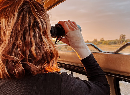 A girl with blonde brown hair, with binoculars in her hands looking for animals on a safari