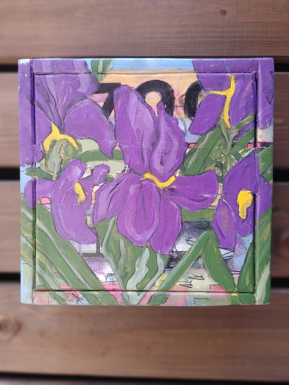 Wooden box painted with vibrant purple and yellow flowers on a wooden table. Text partially visible in the background.