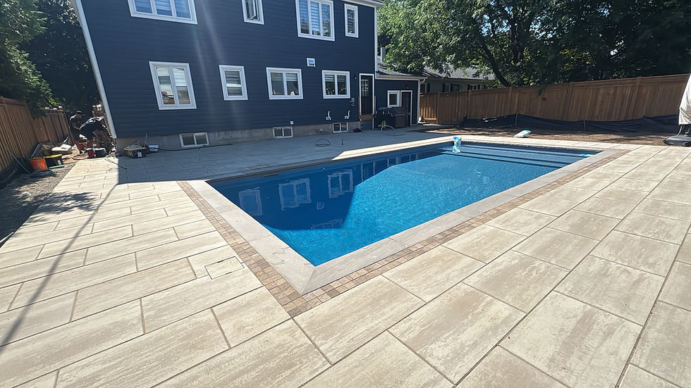 New swimming pool with light patio pavers next to a dark blue house.