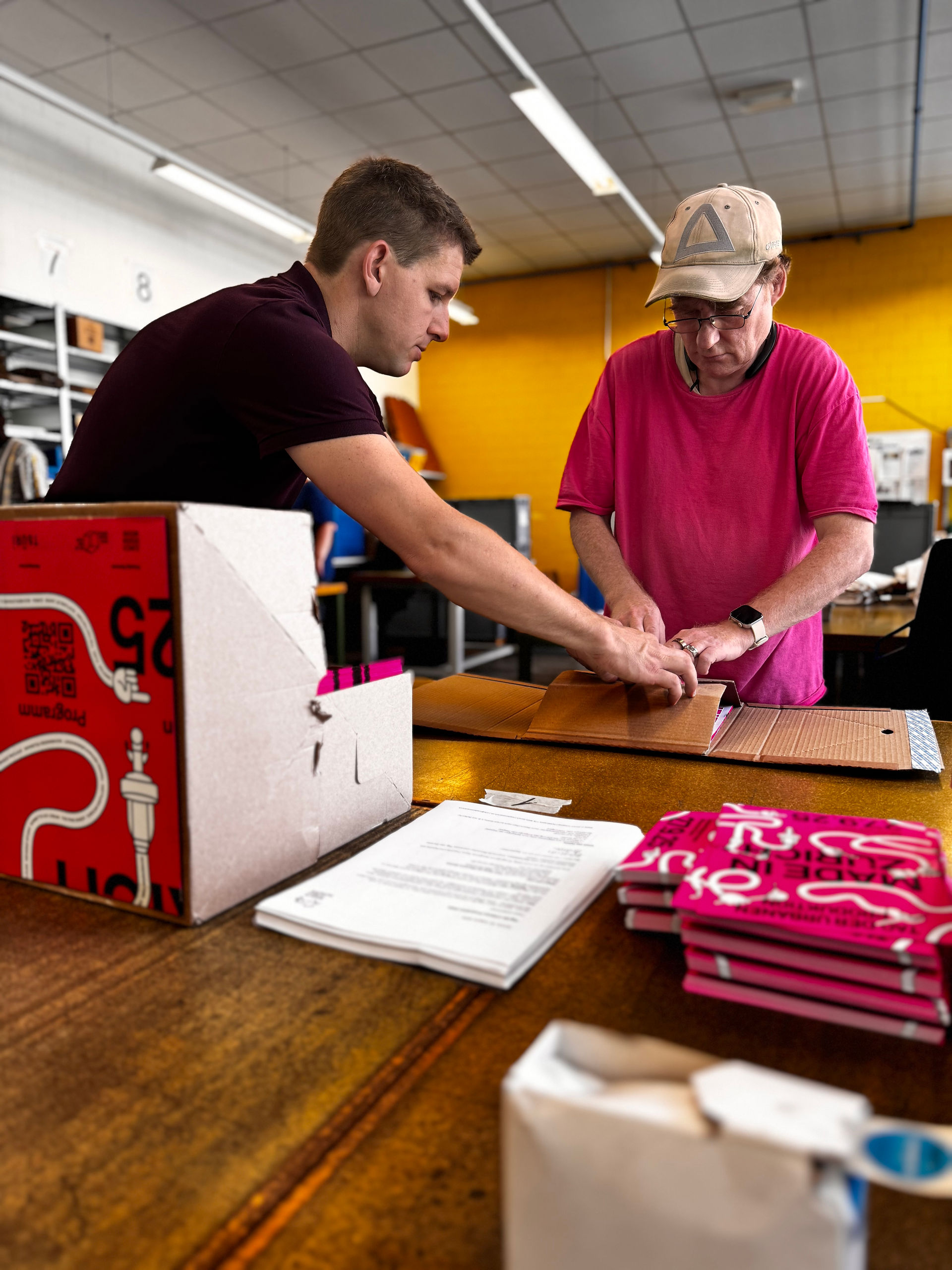Zwei Mitarbeiter der Stiftung Züriwerk falten gemeinsam einen Versandkarton für Werbematerialien des Tags der urbanen Produktion.