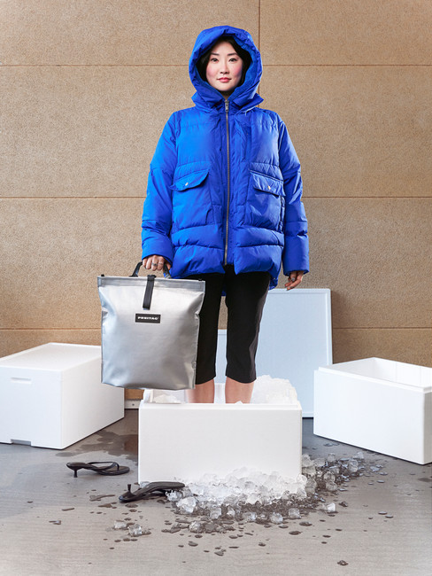 Frau in blauer Jacke mit silbernem F738 COOL BAG von FREITAG zwischen Kühlboxen und Eiswürfeln.