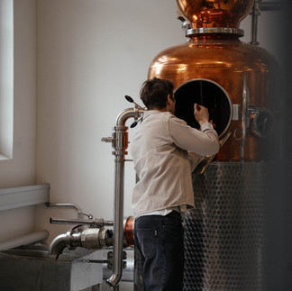 Eine Person arbeitet an einer grossen Kupfer-Brennblase in der Destillerie von Deux Frères in Zürich.