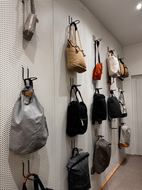 Verschiedene gebrauchte Taschen und Rucksäcke in unterschiedlichen Farben und Formen hängen an einer perforierten weissen Wand im QWSTION Flagship Store.