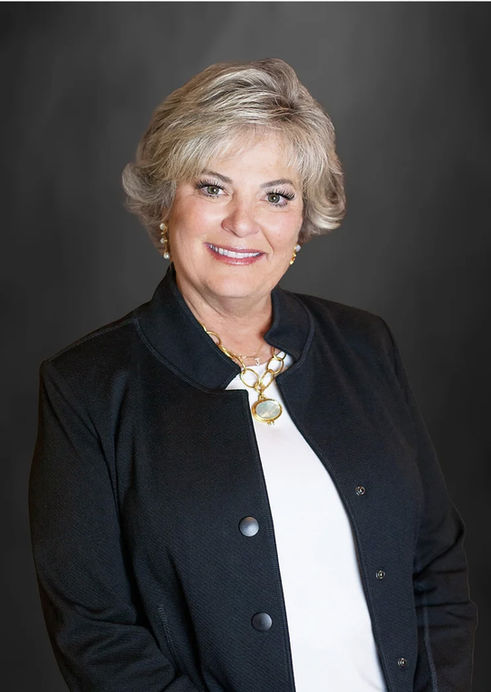 An older businesswoman with short hair, wearing a black blazer and white top, against a dark, solid background. Professional headshot by A Brew and You, Charlotte, NC.