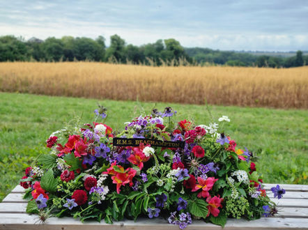 A red white and blue funeral spray of seasonal flowers for a casket with a backdrop of the countryside. 