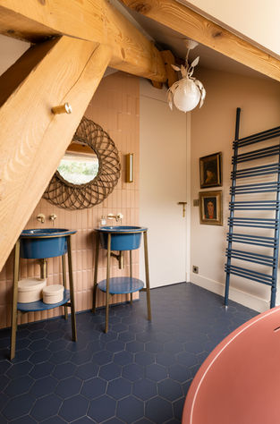 Salle de bain design sous combles avec double vasque bleue et poutres apparentes.