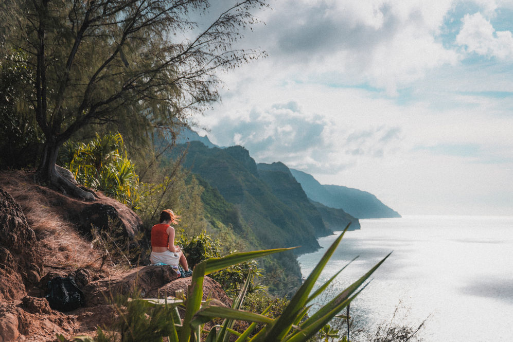 Voyageuse observant la Napali Coast depuis les hauteurs de Kauai, entre océan et végétation luxuriante, un lieu emblématique d’Hawaii.
