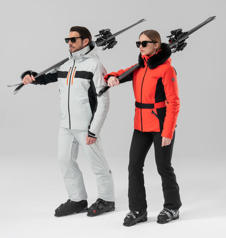 Duo homme et femme en tenues de ski élégantes noir et rouge avec skis sur l’épaule