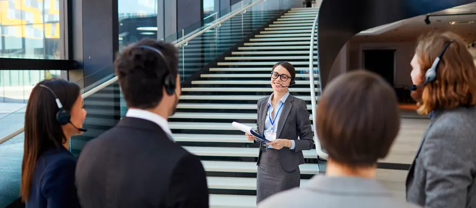 Mulher fala com visitantes através de headset em hall.