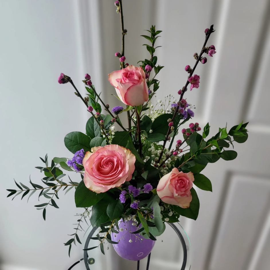 Whimsical bouquet with pink roses, purple accent flowers, and greenery in a free-flowing arrangement