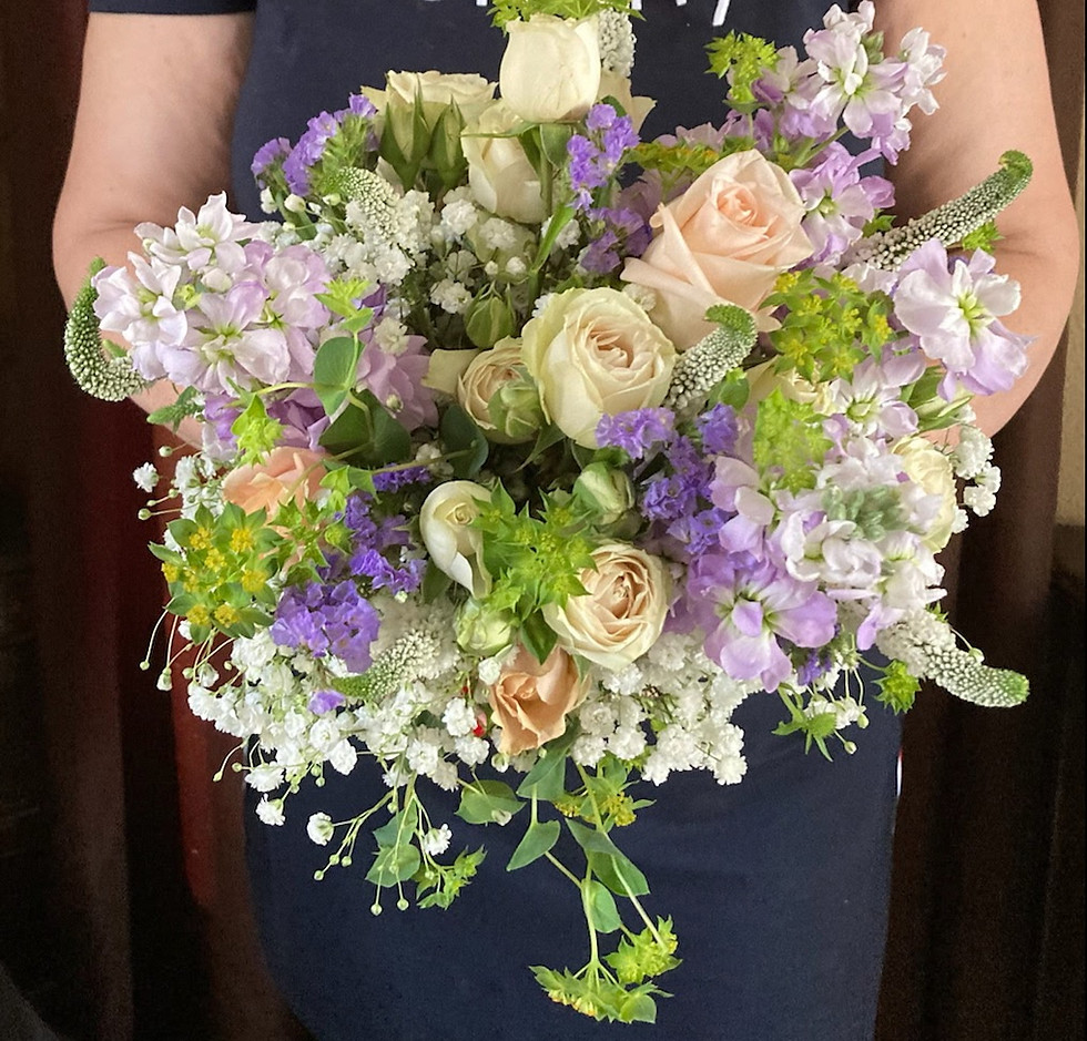 Delicate garden-inspired bouquet with pastel purple blooms, baby pink roses, and lush greenery held in hands