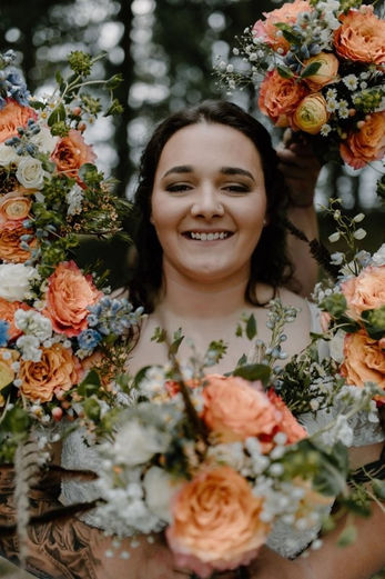 A bride holding her wedding bouquet stands in a serene forest and is surrounded by handcrafted bridesmaid bouquets.