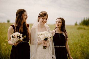 Bride and bridesmaids holding white wedding bouquets with burgundy accents, showcasing elegant bridal florals.