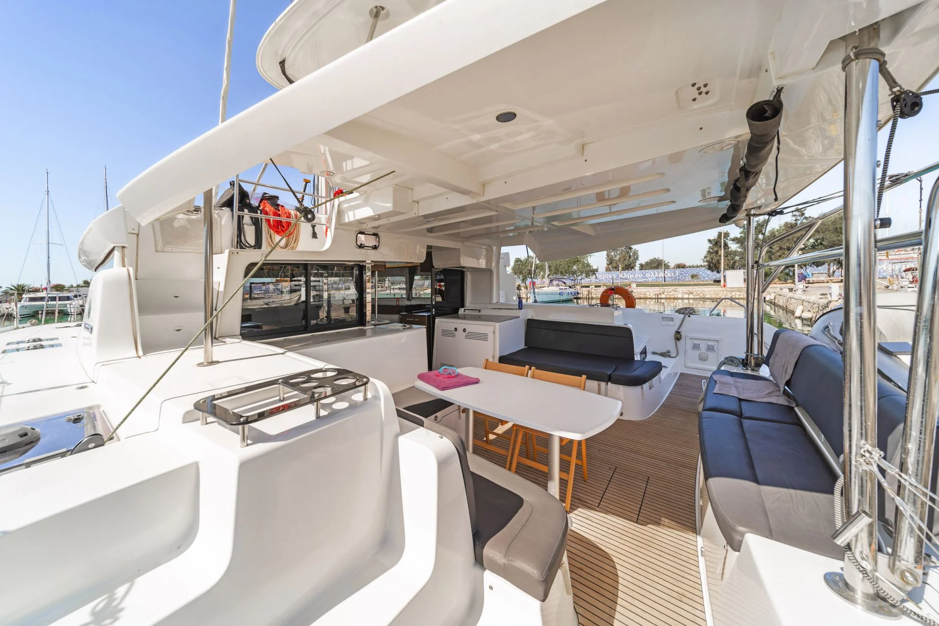 Spacious catamaran cockpit with large central dining table, comfortable shaded seating, outdoor living space for social sailing.